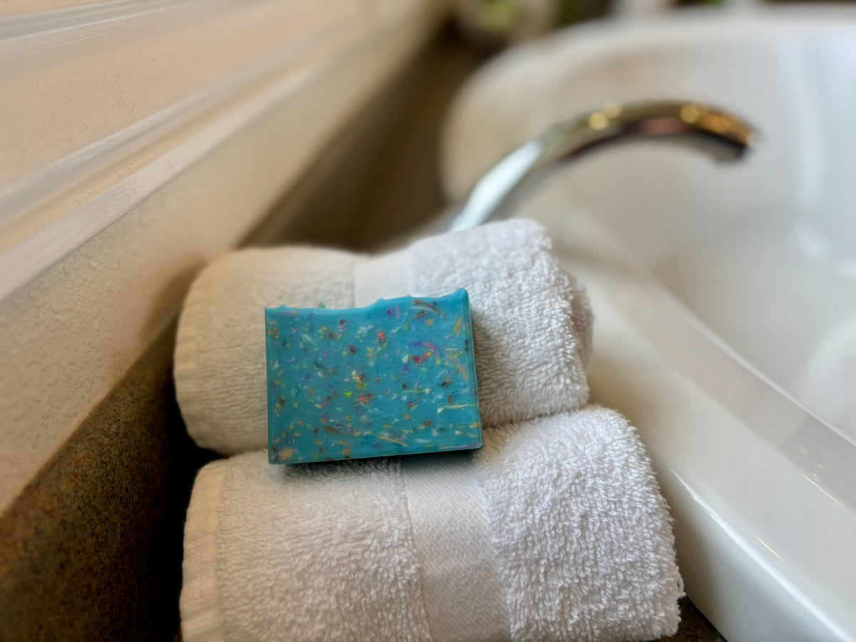 Blue bar soap on rolled white towels in front of a bathtub.