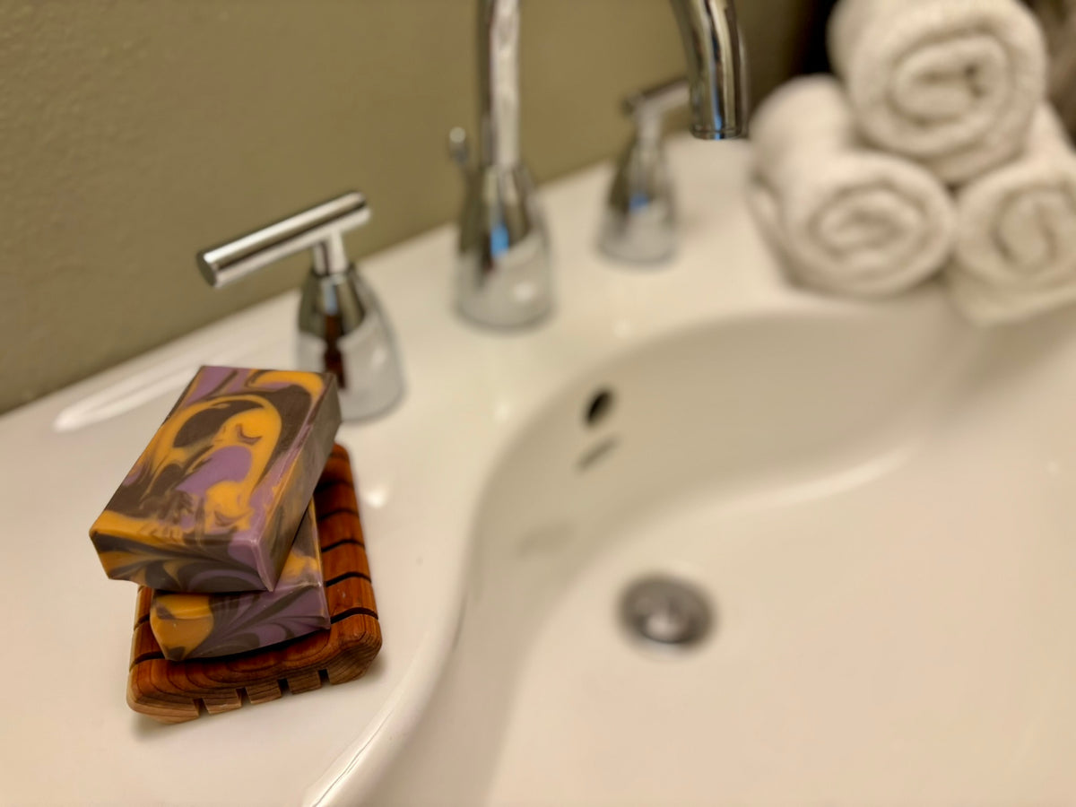 A stack of two marbled soap bars sits on a white bathroom sink next to a chrome faucet, with rolled white towels blurred in the background.