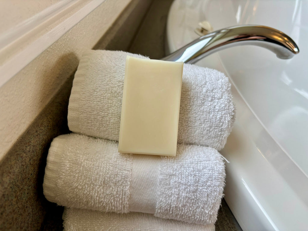 Three folded white towels stacked next to a bathroom sink, with a rectangular bar of soap resting on the top towel.