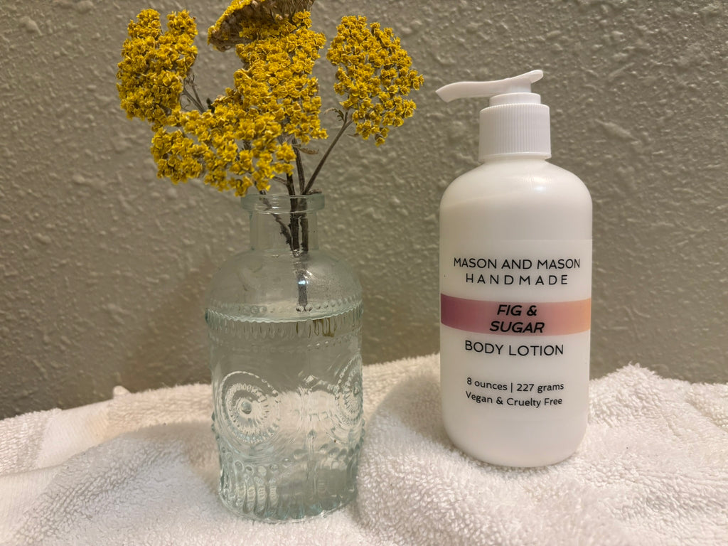 Mason and Mason eight ounce handmade body lotion bottle with a pump, next to a vase of yellow flowers on a towel.