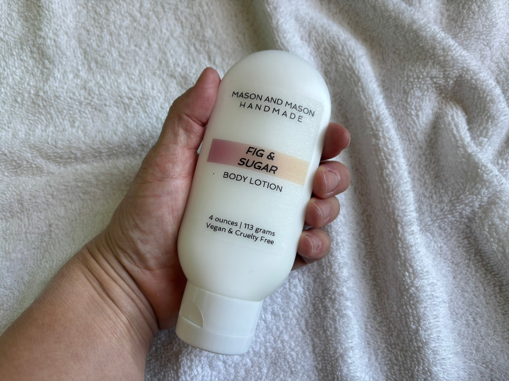 Hand holding a four ounce ebottle of Mason and Mason Handmade Fig & Sugar body lotion against a textured white background