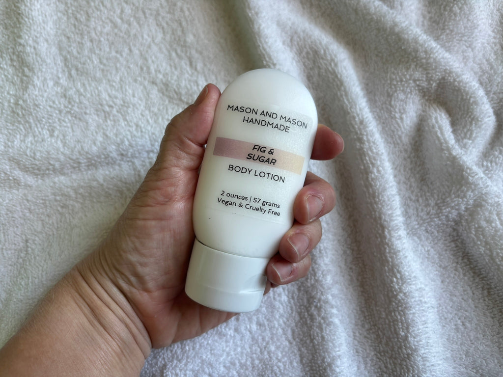 Hand holding a two ounce Mason and Mason body lotion bottle against a textured white background