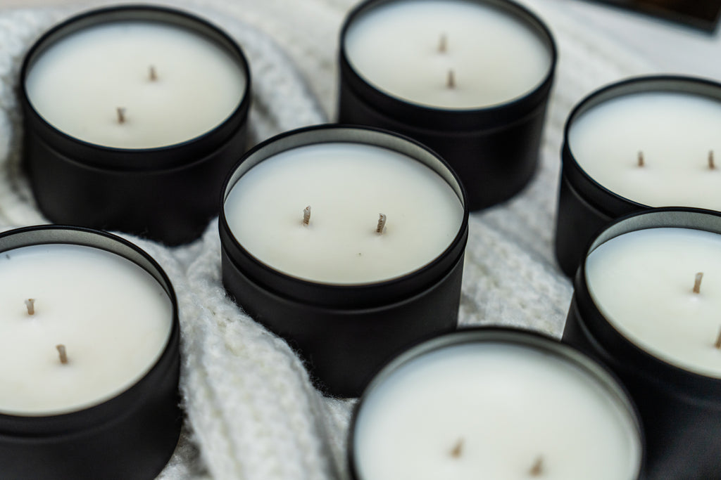 Several black metal tin candles with white wax are arranged closely together on a white knit blanket.