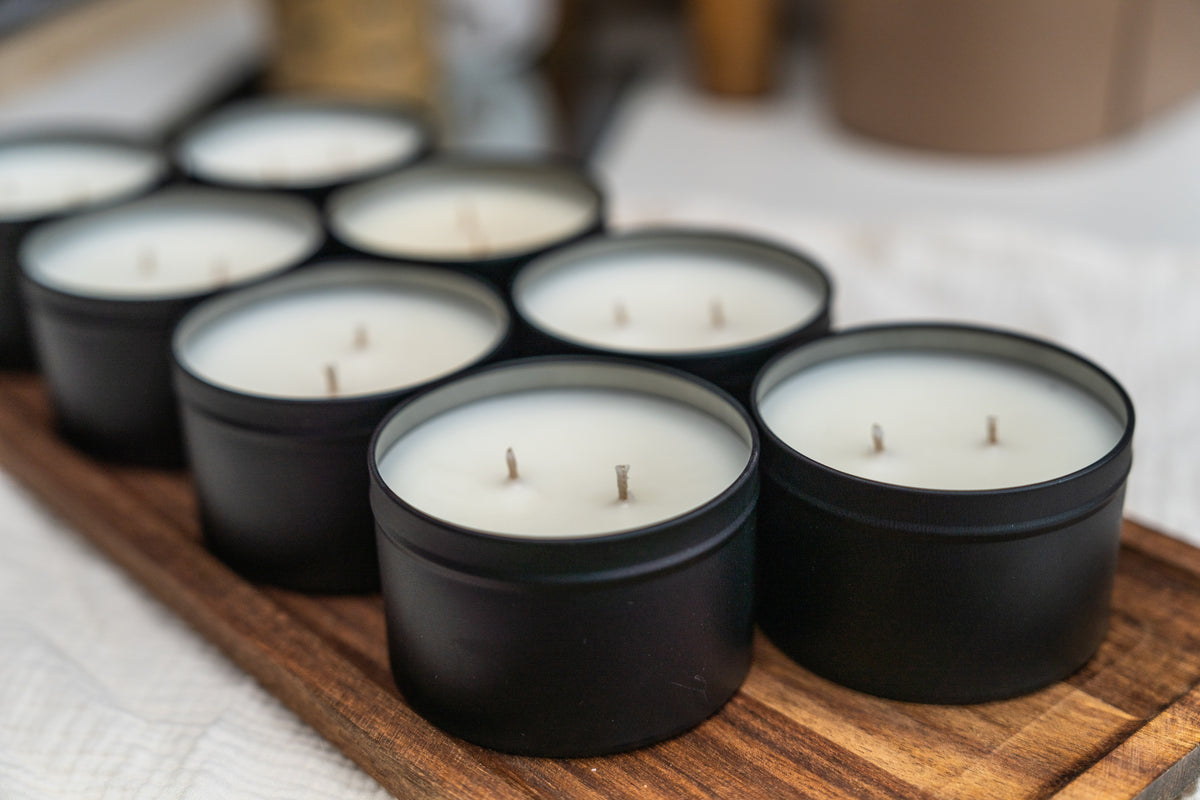 Several small black tin candles with white wax are arranged on a wooden tray in a softly blurred indoor setting.