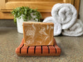 Marbled soap bar on a wooden soap dish with towels and a plant in the background.