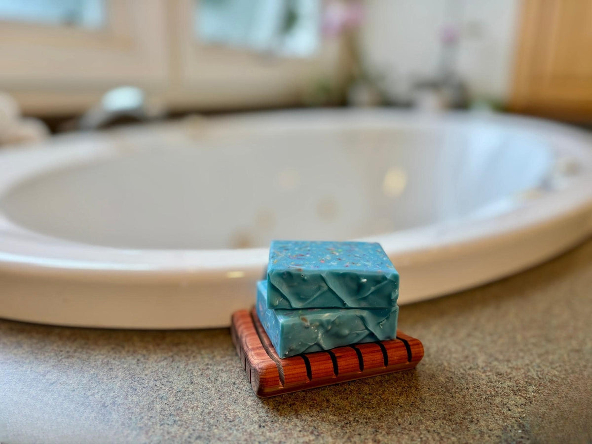 Two blue soap bars on a wooden soap dish in front of a bathtub.