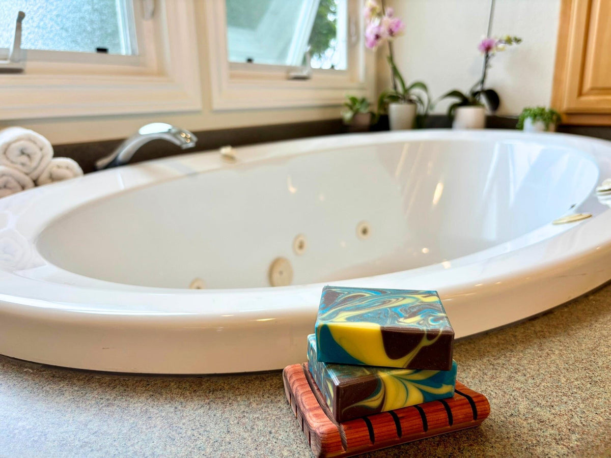 Colorful soap bars on a wooden dish in front of a white bathtub.