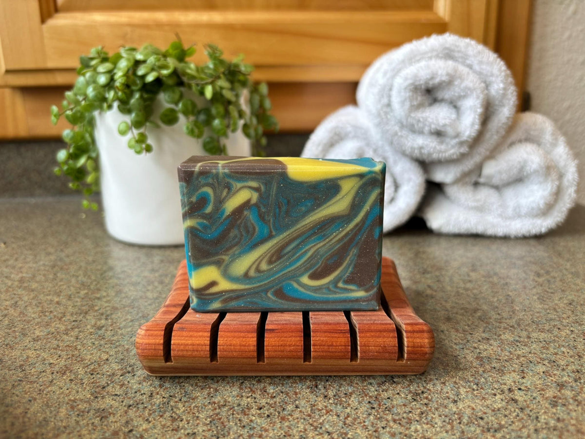 Marbled soap bar on a wooden dish with towels and a plant in the background