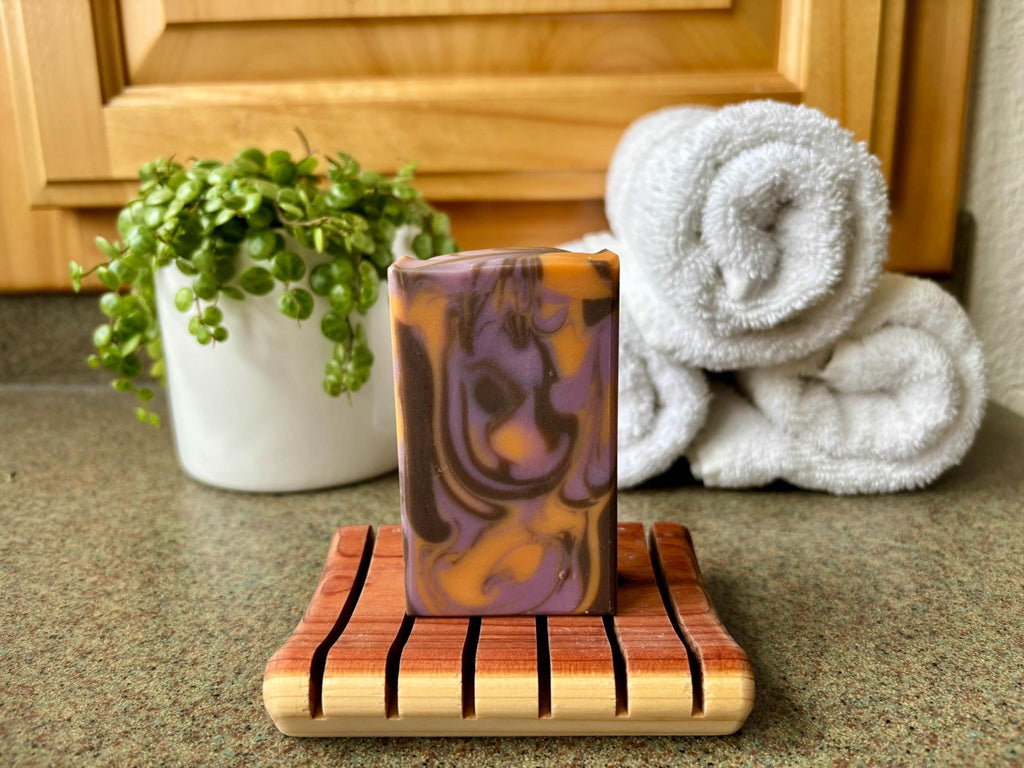 Bar of soap on a wooden stand with towels and a plant in the background