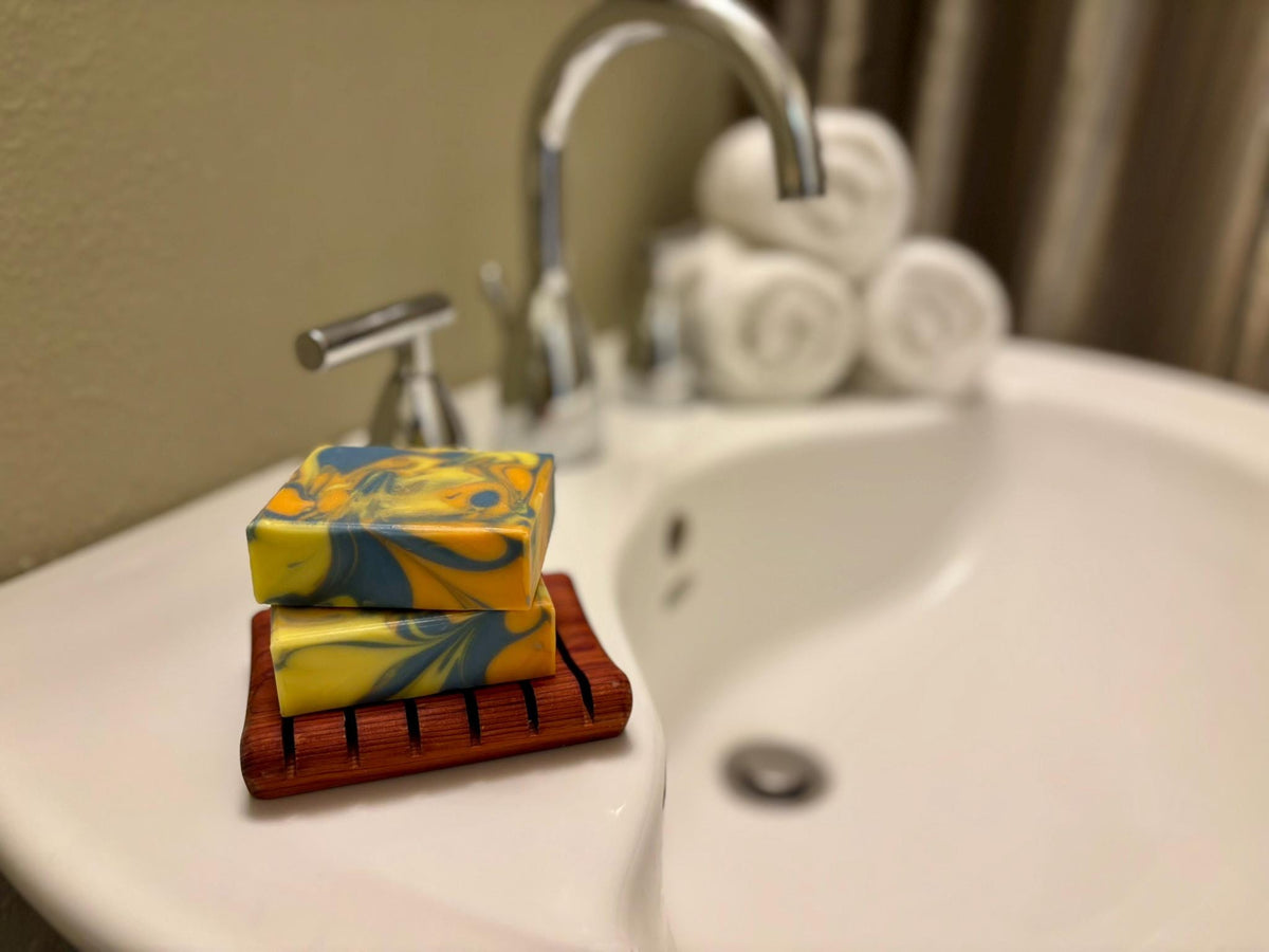 Two colorful soap bars on a wooden soap dish in front of a sink.