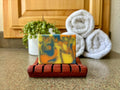 Colorful soap on a wooden stand with towels and a plant in the background