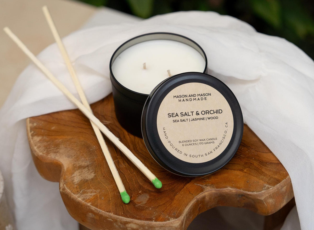 Mason and Mason handmade candle with sea salt and orchid scent on a wooden coaster with match sticks.