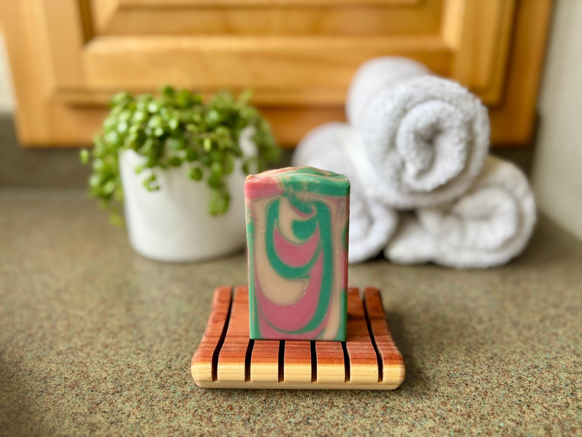 Colorful soap bar on a wooden dish with towels and a plant in the background
