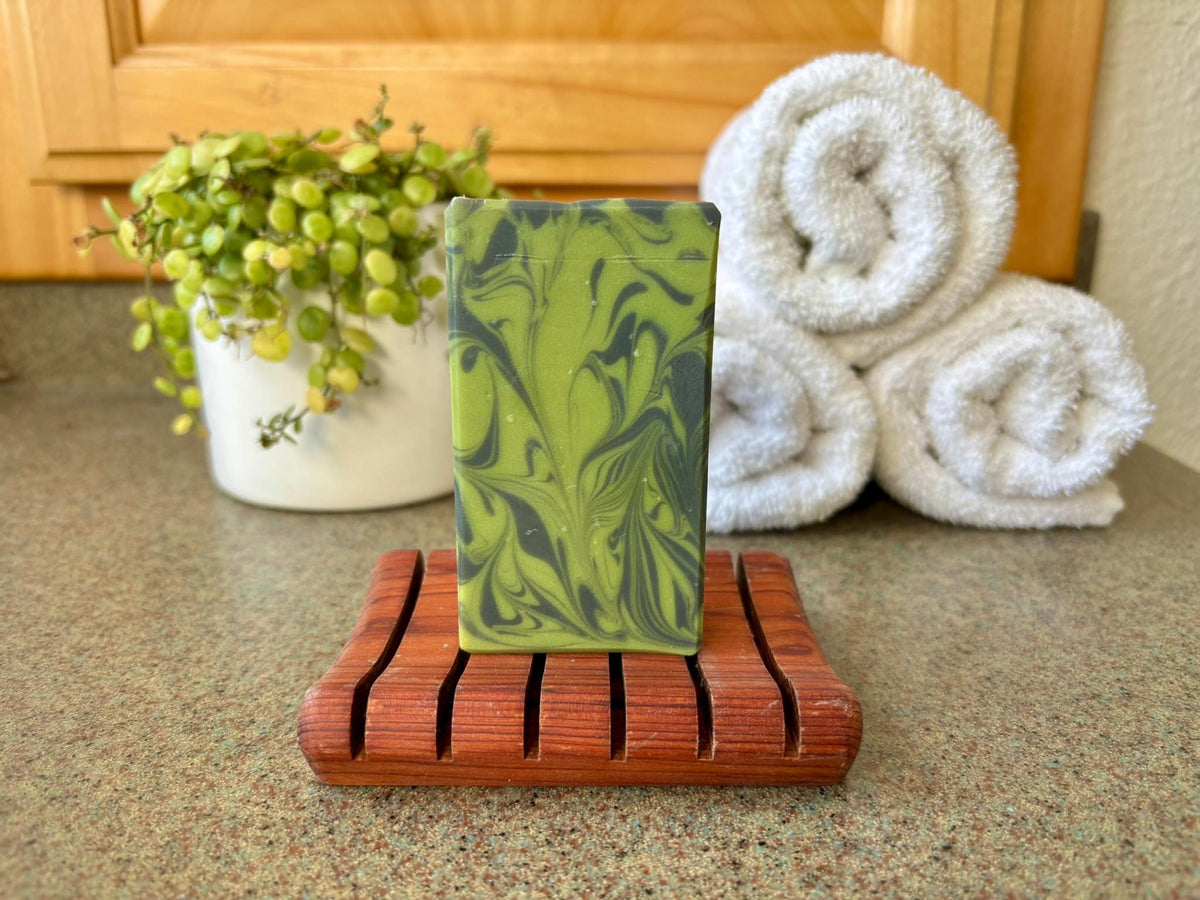 Green marbled soap on a wooden dish with rolled towels and a plant in the background.