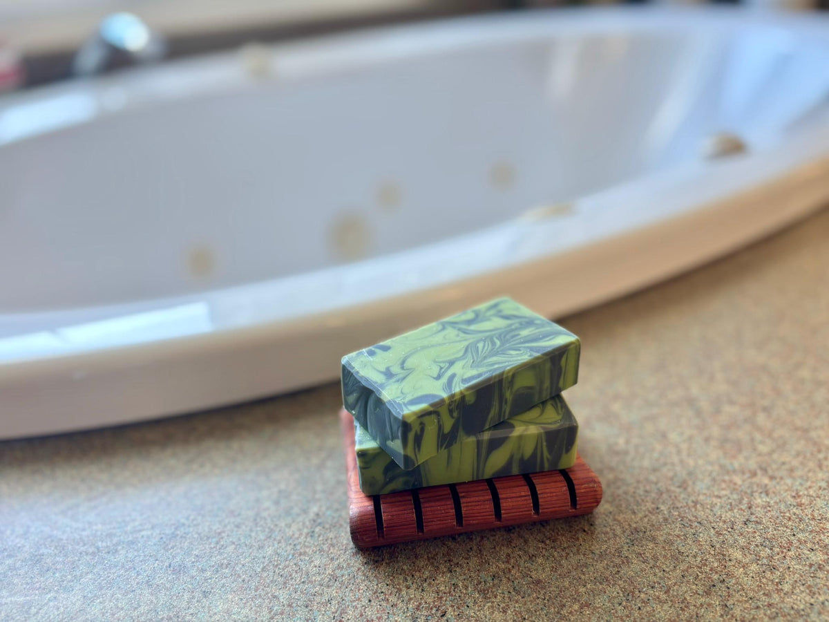 Two green marbled soap bars stacked on a wooden dish with a blurred background.