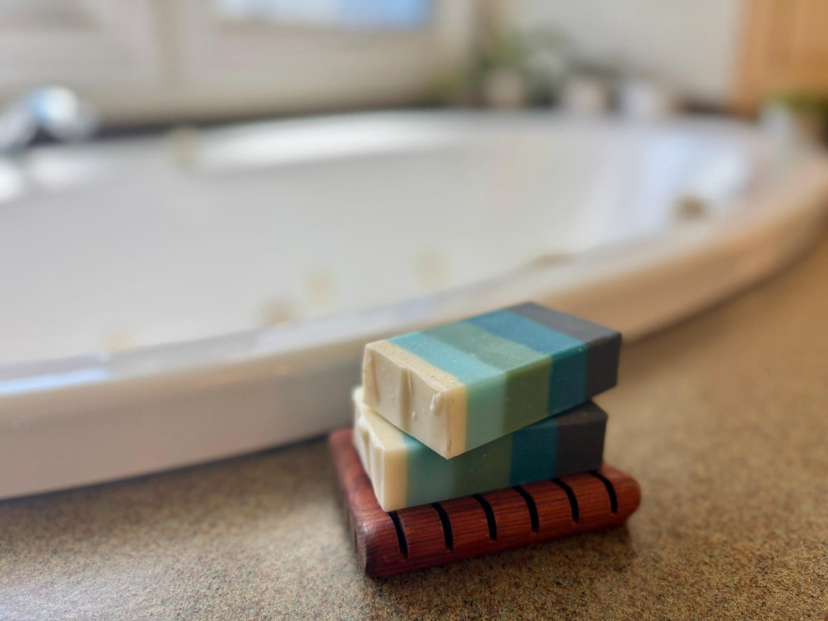 Stack of colorful soap bars on a wooden soap dish with a blurred bathroom background