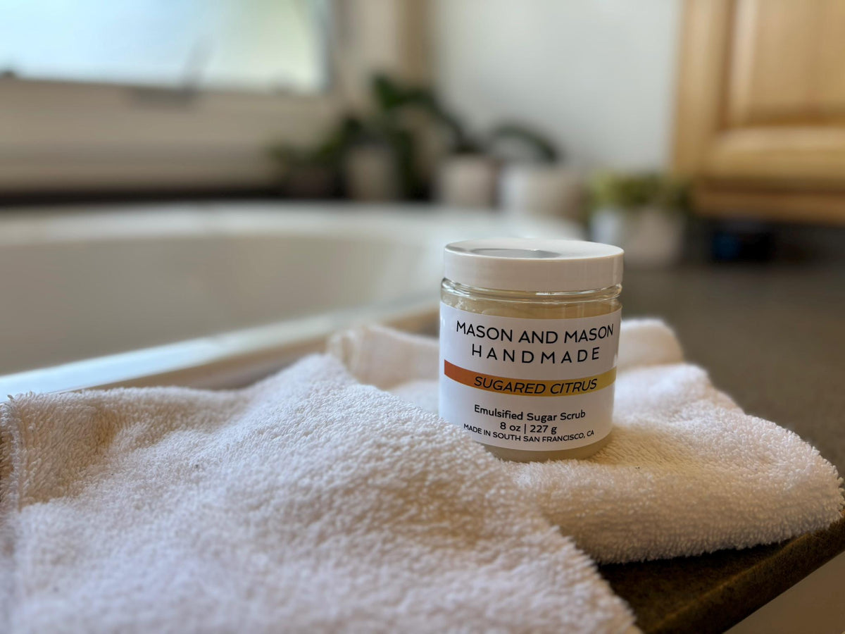 Jar of 'Mason and Mason Handmade' sugar scrub on a towel with a blurred background