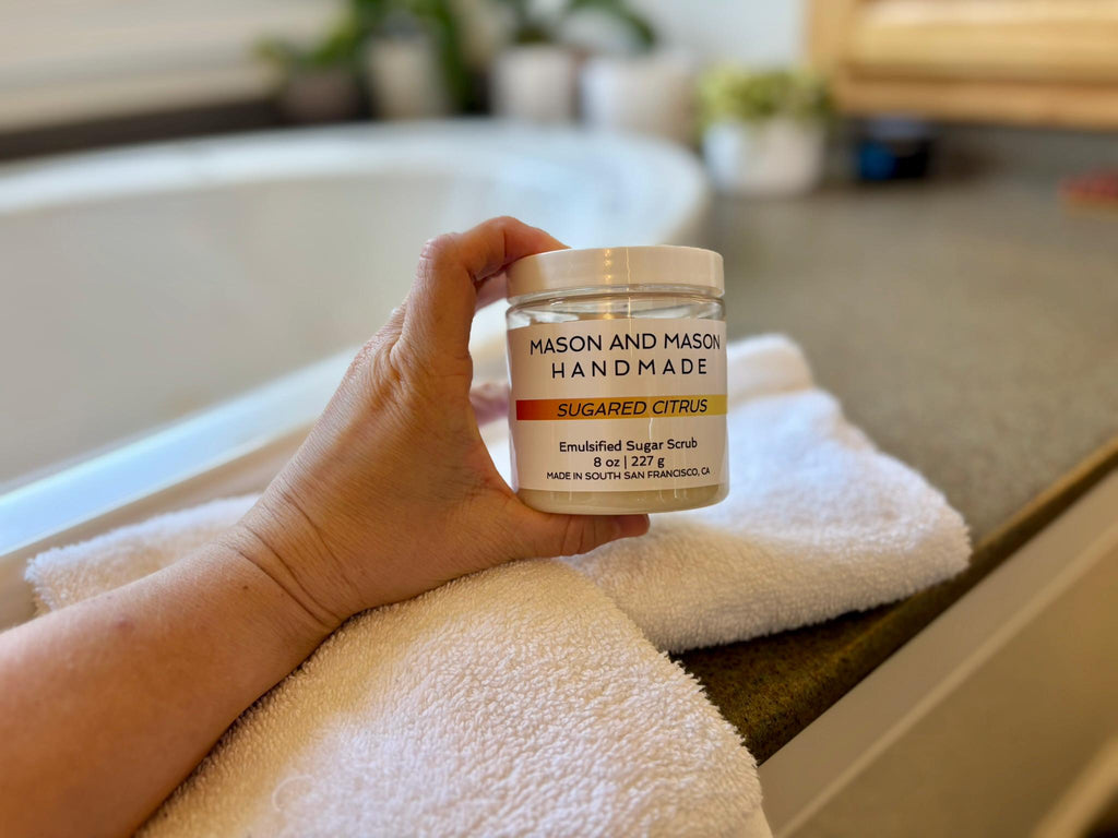 Hand holding a jar of Mason and Mason handmade sugar scrub on a bathroom counter.